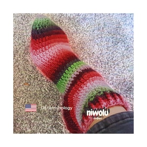 May include: A handmade crochet sock in shades of red, green, pink, and brown. The sock is striped and appears to be warm and cozy. The sock is on a light-colored carpet. The brand name "niwolu creations" is visible.