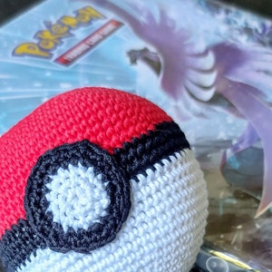May include: A crocheted Poké Ball made with red, white and black yarn. The Poké Ball is a popular item in the Pokémon franchise.