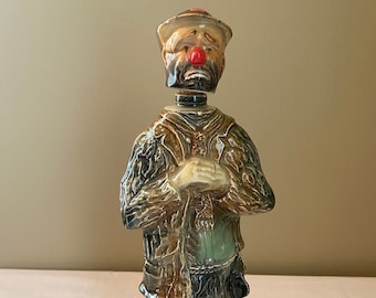 Puede incluir: Una decantador de cerámica con forma de payaso triste con nariz roja y barba marrón. La decantador está etiquetada "The Original Emmett Kelly Beam 1,75 Litros 80 Proof Kentucky Straight Bourbon Whiskey".