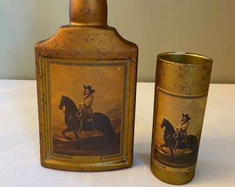 Op de afbeelding: Een gouden glazen fles met een zwarte dop en een gouden glazen tumbler. Beide hebben een gedrukt beeld van een man op een paard. De afbeelding is omgeven door een gouden kader. De tekst "Man on a Horse" is gedrukt op de bodem van de fles en de tumbler.