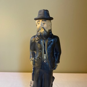 Pode incluir: Uma figurinha de cerâmica de Devil Anse Hatfield, uma figura famosa da disputa Hatfield-McCoy, segurando um rifle. A figurinha é uma garrafa para Beam 1795 Kentucky Straight Bourbon Whiskey.