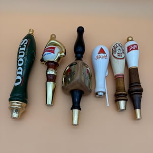 Puede incluir: Colección de seis tiradores de grifo de cerveza. Los tiradores presentan varios diseños, incluyendo el logotipo de "O'Doul's", un tirador dorado y rojo de "Budweiser", un tirador de madera de "Michelob", un tirador blanco de "Bass", un tirador de "George Killian's Irish Red" y un tirador de "Schlitz".