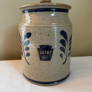 Puede incluir: Un tarro de cerámica con un diseño azul y blanco. El tarro tiene una tapa y está decorado con un logotipo de Heinz 57.