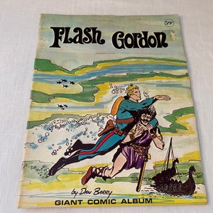 Könnte beinhalten: Ein Vintage-Comic-Cover mit Flash Gordon, einem Science-Fiction-Helden, in einer dramatischen Szene. Die Cover-Illustration zeigt Flash Gordon in blauer Uniform, der einen Mann in brauner Tunika hält, mit einem Wikingerschiff im Hintergrund. Der Covertext lautet "Flash Gordon" und "Giant Comic Album" von Dan Barry.