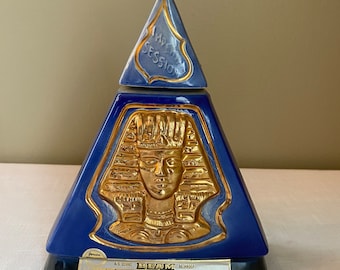 Puede incluir: Una decantador de cerámica azul y dorado con forma de pirámide con un diseño de faraón egipcio. La etiqueta dice "Beam 100 Months Old Kentucky Straight Bourbon Whiskey".