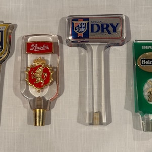 May include: Four clear plastic beer tap handles with different brand logos. The logos are Old Style, Stroh's, Old Style Special Dry, and Heineken.