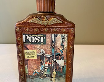 May include: A brown glass bottle with a wooden stopper and a label that reads "Beam Bicentennial Bourbon 100". The bottle is decorated with a picture of a magazine cover from The Saturday Evening Post, dated May 26, 1945, featuring a Norman Rockwell painting of a neighborhood scene.