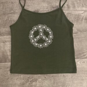 May include: A green tank top with a white peace sign made of flowers.