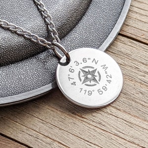 May include: Silver necklace with a round pendant featuring a compass rose and the coordinates 47.6'3.6" N 119° 59.42' W.
