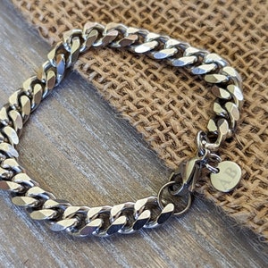 May include: A silver curb chain bracelet with a clasp and a small round tag engraved with the letters "AB".