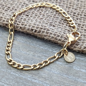 Peut inclure: Un bracelet en chaîne dorée avec un petit charme rond gravé des initiales "JT".