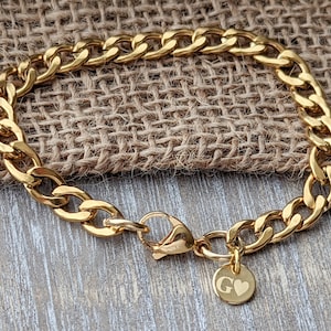 May include: A gold chain bracelet with a curb link design and a small charm with the letter "G" and a heart.