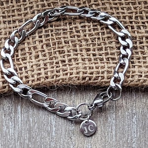 May include: A silver curb chain bracelet with a small charm that says "JC" on it.