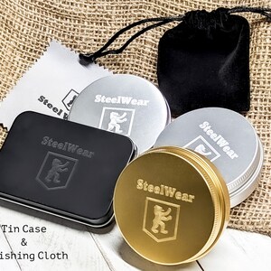 May include: A set of four metal tins with the logo "SteelWear" and a lion emblem. The tins are in gold, silver, and black. The set also includes a black velvet pouch and a polishing cloth.
