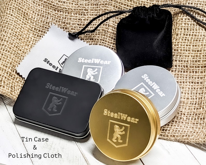 May include: A set of four metal tins with the logo "SteelWear" and a lion emblem. The tins are in gold, silver, and black. The set also includes a black velvet pouch and a polishing cloth.