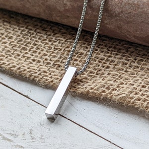 May include: A silver bar pendant necklace with a delicate chain. The pendant is a simple, rectangular shape.