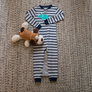May include: A gray and blue striped pajamas with a dinosaur graphic on the front. A brown stuffed dog is lying on the pajamas.
