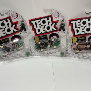 May include: Three Tech Deck finger skateboards in packaging. Each package features the "Demon Slayer" logo and a graphic of a character with a sword. The skateboards have unique designs and are numbered 1/3, 2/3, and 3/3.