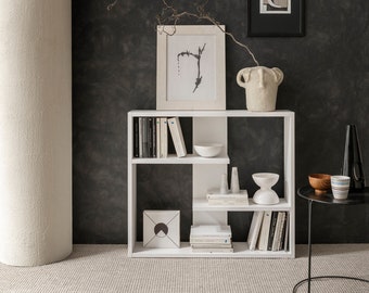 May include: White bookshelf with five shelves, featuring books, a vase, and framed artwork. The bookshelf is against a dark gray wall.