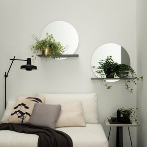 K&ouml;nnte beinhalten: Ein wei&szlig;es Schlafzimmer mit einem Bett, zwei runden Spiegeln mit Regalen und einer schwarzen Stehlampe. Die Spiegel h&auml;ngen an der Wand und haben Pflanzen auf den Regalen. Es gibt einen kleinen schwarzen Beistelltisch mit einer Pflanze darauf.