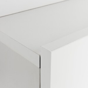 Pu&ograve; includere: Primo piano di un armadio bianco con una superficie liscia e piatta. L'armadio ha un design semplice e moderno con linee pulite e bordi netti.