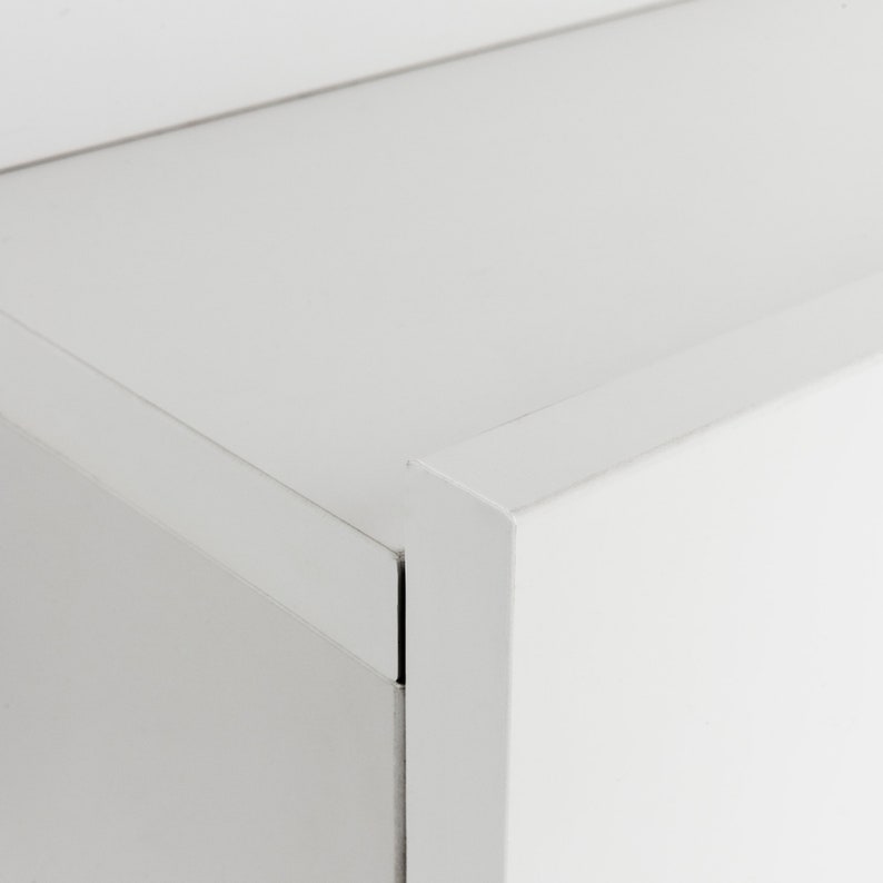 Pu&ograve; includere: Primo piano di un armadio bianco con una superficie liscia e piatta. L'armadio ha un design semplice e moderno con linee pulite e bordi netti.