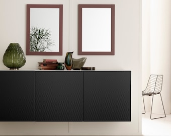 May include: A black cabinet with three doors, a white countertop, and two framed mirrors with maroon frames. The cabinet is decorated with a green glass vase, a brown glass vase, a small green vase, a stack of books, and a silver tray with a decorative object.