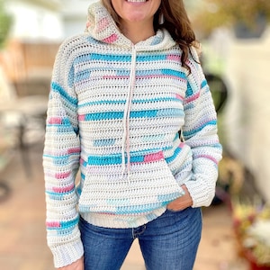 May include: A handmade crochet hoodie in a cream color with horizontal stripes of light blue and pink. The hoodie has a drawstring and a front pocket. The sleeves are long, and the hood is lined with the same striped pattern.