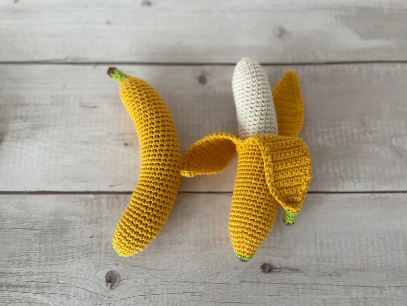 May include: Two crocheted banana toys. One banana is yellow and has a green stem. The other banana is white and has a yellow peel.