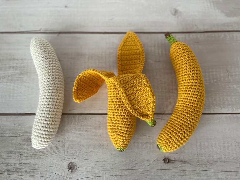 May include: Three crocheted banana toys. One is white, and two are yellow. The yellow bananas are in a curved shape, and the white banana is straight.