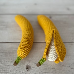May include: Two crocheted banana toys. One banana is yellow and has a green stem. The other banana is yellow and has a green stem and is partially peeled to reveal a white crocheted inside.
