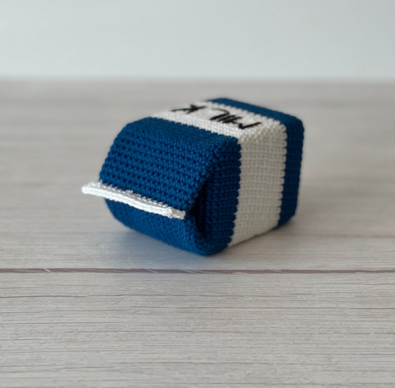 May include: A crocheted milk carton toy in blue and white. The carton has the word "MILK" stitched on the side.
