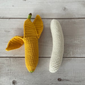May include: Two crocheted bananas, one yellow and one white, on a light wood background.