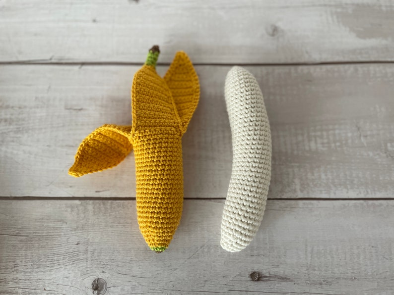 May include: Two crocheted bananas, one yellow and one white, on a light wood background.