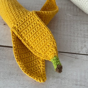 May include: A crocheted banana toy with a yellow body, green stem, and brown tip. The banana is curled into a crescent shape.