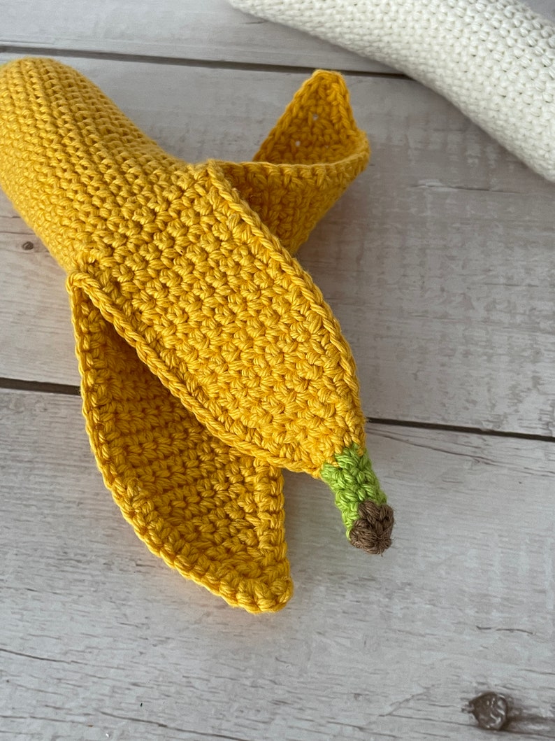 May include: A crocheted banana toy with a yellow body, green stem, and brown tip. The banana is curled into a crescent shape.
