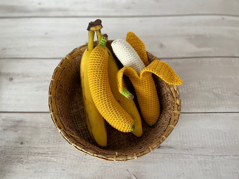 May include: Three crocheted bananas in a woven basket. Two are yellow and one is white.