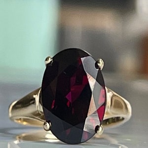 May include: A gold ring with a large, oval-shaped, dark red gemstone.