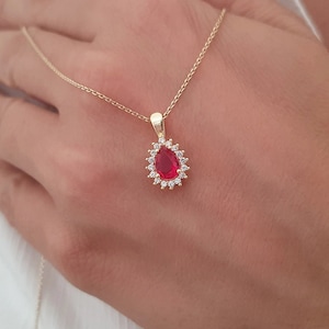May include: A gold chain necklace with a red pear-shaped gemstone pendant surrounded by a halo of smaller clear gemstones.