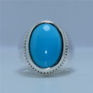 May include: A silver ring featuring a large oval turquoise gemstone set in a bezel setting. The ring has a decorative border around the stone.