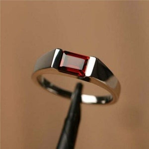 May include: A silver band ring with a rectangular red gemstone.