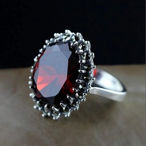 May include: A silver ring with a large, red gemstone surrounded by a band of black marcasite stones.