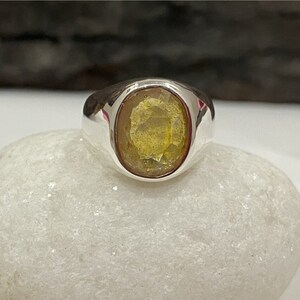 May include: A silver ring with a yellow oval gemstone set in a bezel setting.