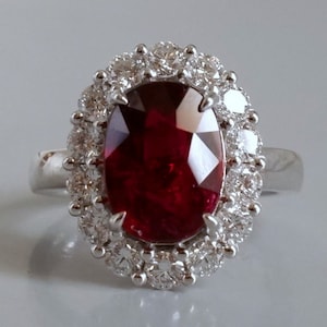 Op de afbeelding: Een zilveren ring met een grote ovale robijn, omringd door een halo van kleinere diamanten.