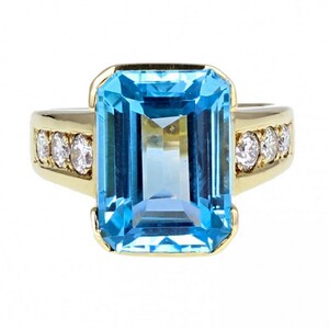 May include: A gold ring with a large, emerald-cut blue topaz gemstone and a band of smaller diamonds.