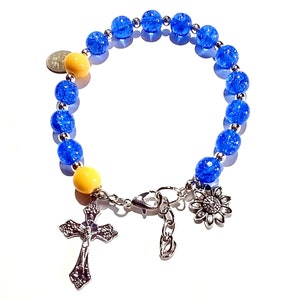 May include: A blue and yellow beaded bracelet with a silver cross, sunflower charm, and clasp.