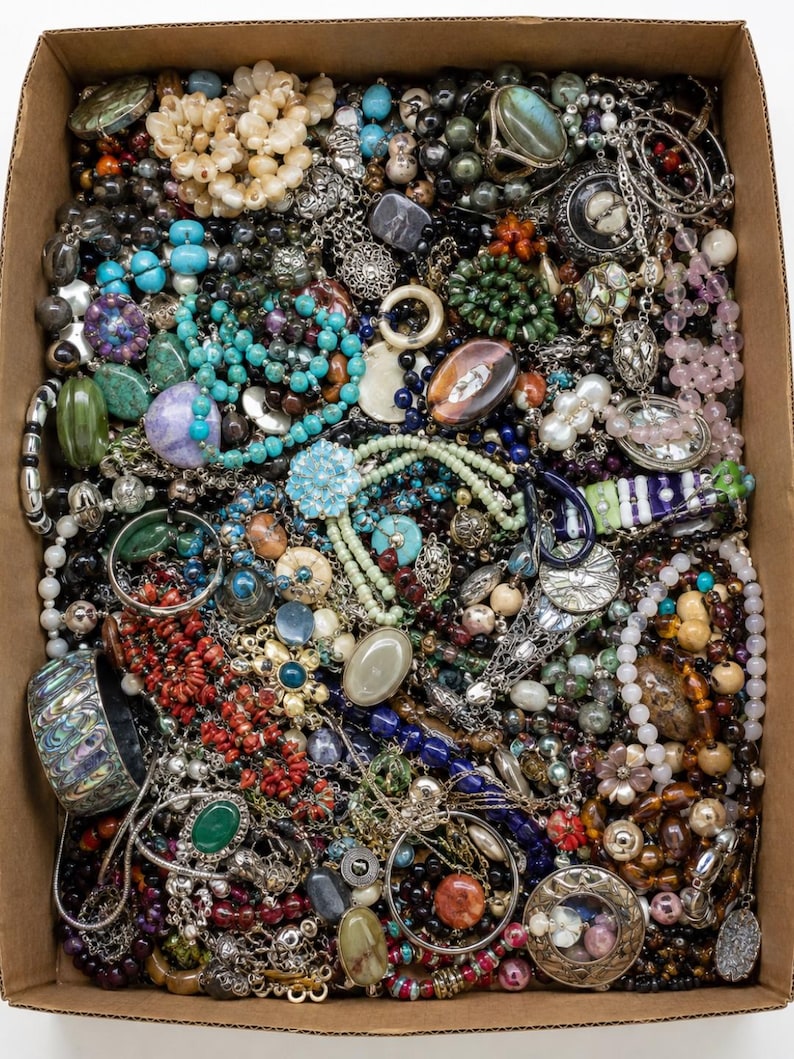 May include: A large cardboard box filled with a diverse collection of costume jewellery, including various beaded necklaces, metal chains, bracelets, rings, and pendants in assorted colours, textures, and materials like glass, stone, and metal.