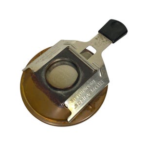 May include: A vintage, circular metal object with a black handle and a silver-colored metal frame. The object has a bronze-colored base and the text "Nur auffüllen mit Spring firestar" is visible on the frame.