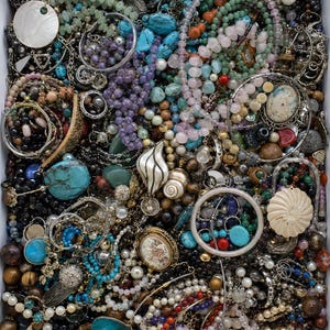 May include: A large collection of assorted jewellery pieces packed into a rectangular box, including various beaded necklaces, metal chains, turquoise stones, pearl strands, shell pendants, and intricate brooches in a mix of colours and textures.
