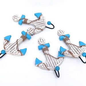 Puede incluir: Cuatro ancras de madera blanca con detalles azules y de cuerda. Cada ancla tiene un gancho de metal negro para colgar.